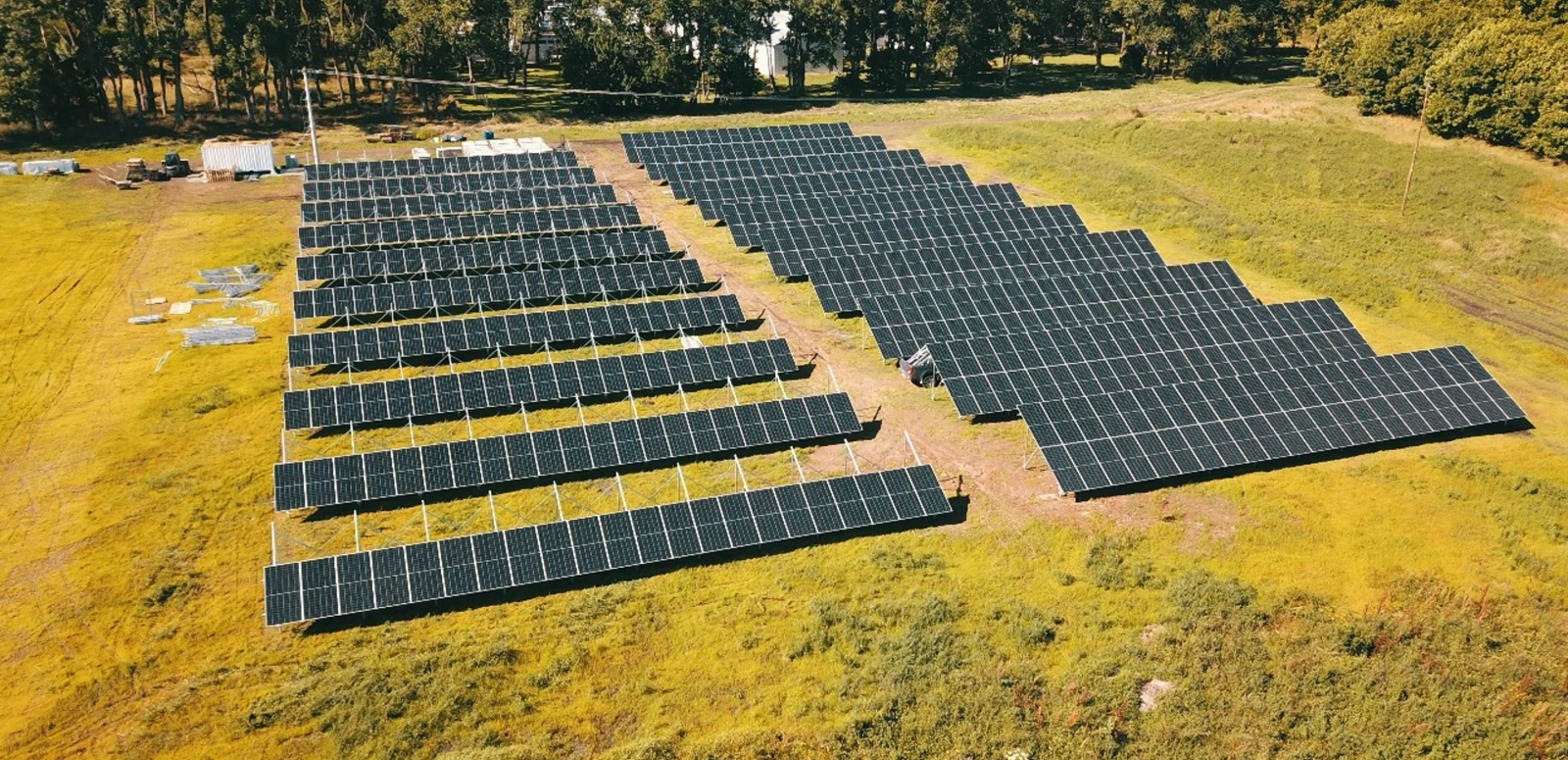 An aerial view of a large ground-mounted solar array in a grassy field for an industrial project.