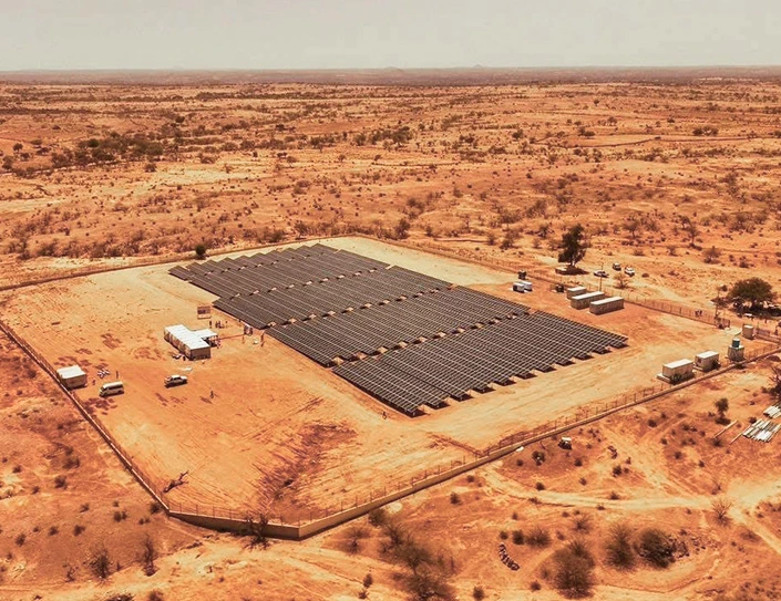 Aerial view of a large solar farm with rows of blue photovoltaic panels set in a remote, arid landscape in Chad.